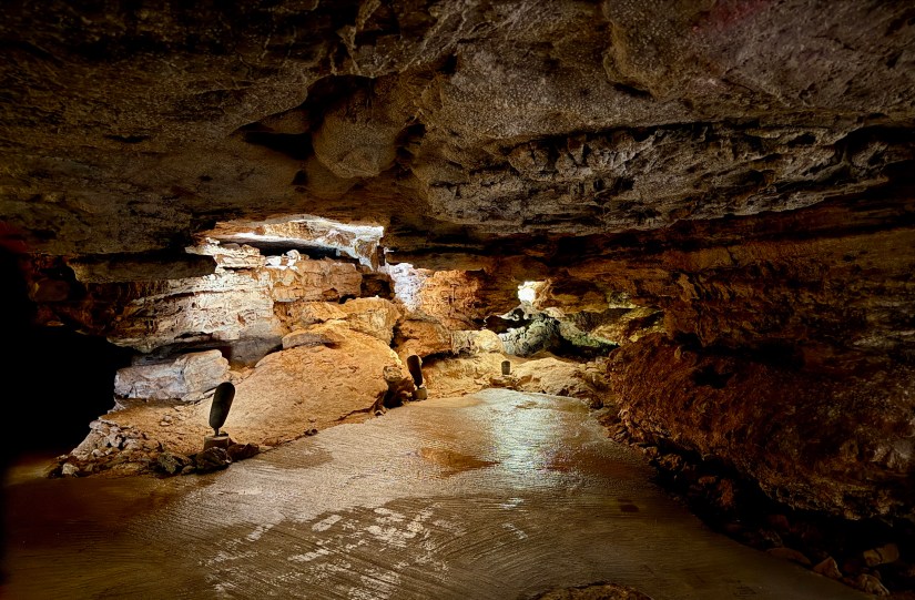 Interior view of Wind Cave showing textured rock formations and floor with lighting highlighting the natural features.