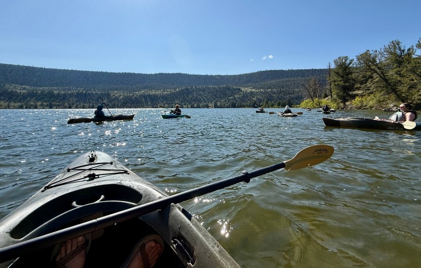 View from a kayak on Trail Lake, showcasing participants engaging in kayaking amidst scenic mountains and clear blue skies.