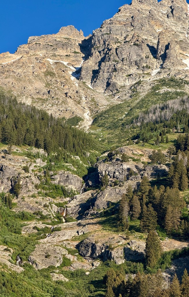 A rugged mountain landscape featuring rocky peaks and patches of greenery, under a clear blue sky.