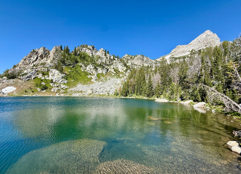 A serene alpine lake surrounded by rugged mountains and lush greenery under a clear blue sky.