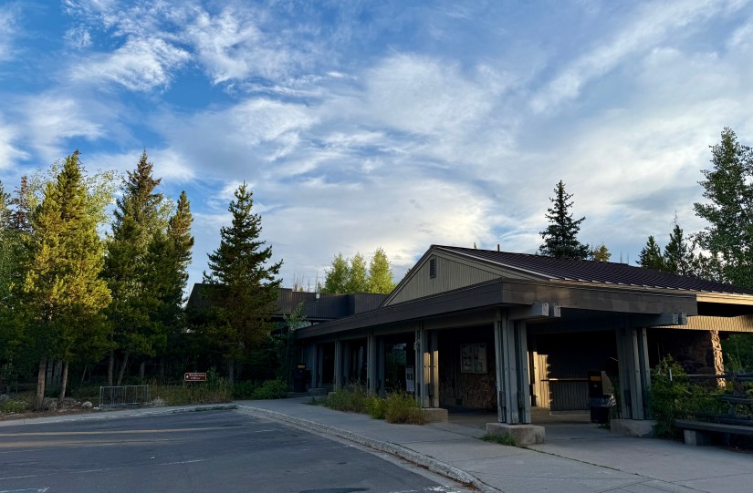 A visitor center building surrounded by green trees under a blue sky with scattered clouds.