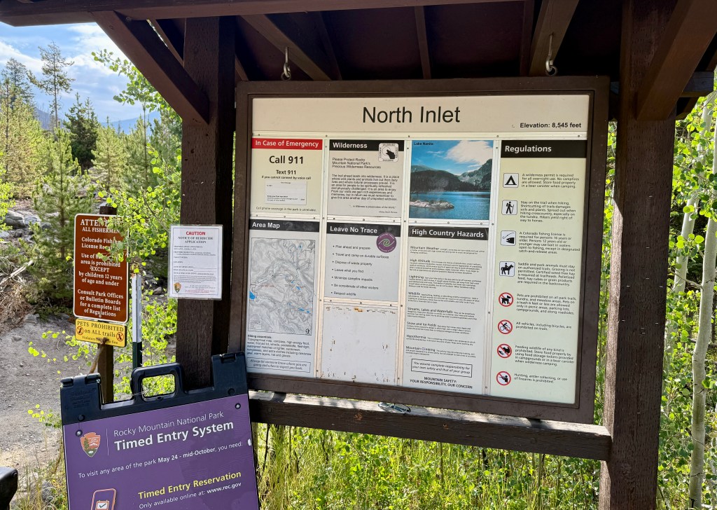 Signpost at the North Inlet Trailhead in Rocky Mountain National Park, featuring regulations and emergency information.