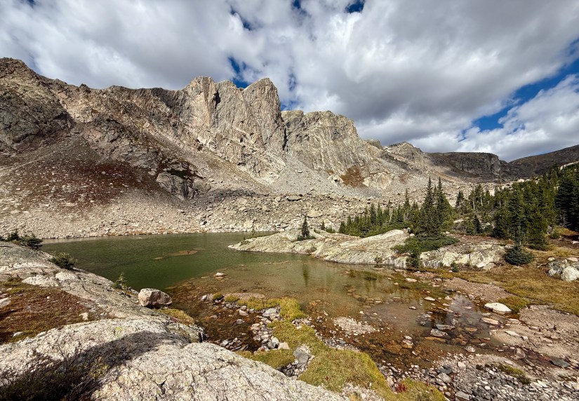 A scenic view of Mirror Lake surrounded by mountainous terrain, featuring rocky cliffs and patches of trees under a partly cloudy sky.