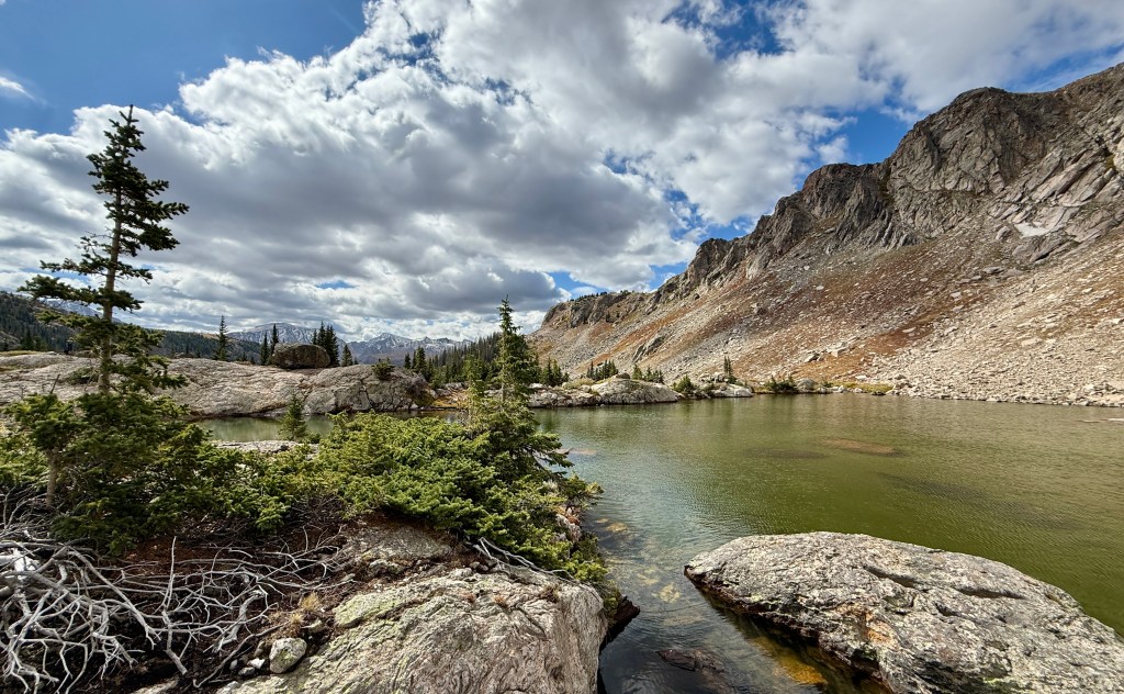A scenic view of Mirror Lake in Rocky Mountain National Park, surrounded by rocky mountains and lush green foliage under a partly cloudy sky.