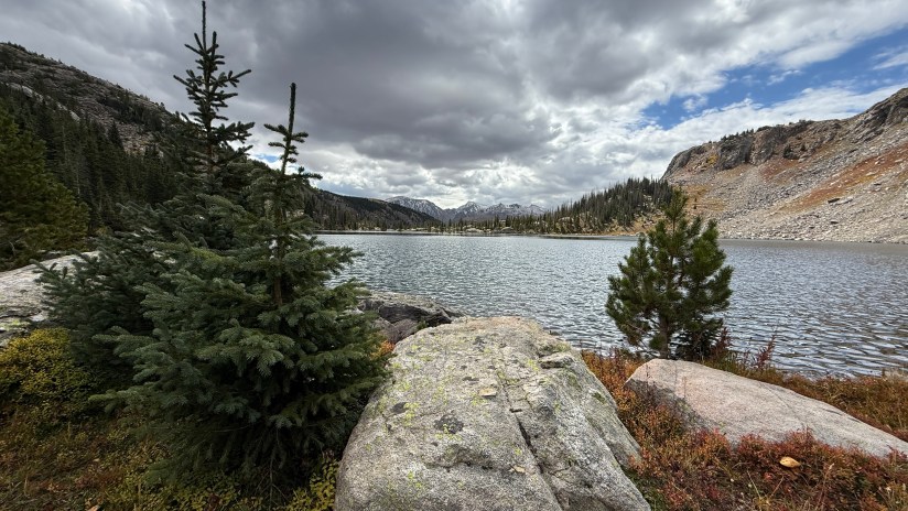 View of Mirror Lake surrounded by rocky terrain and pine trees under a cloudy sky.