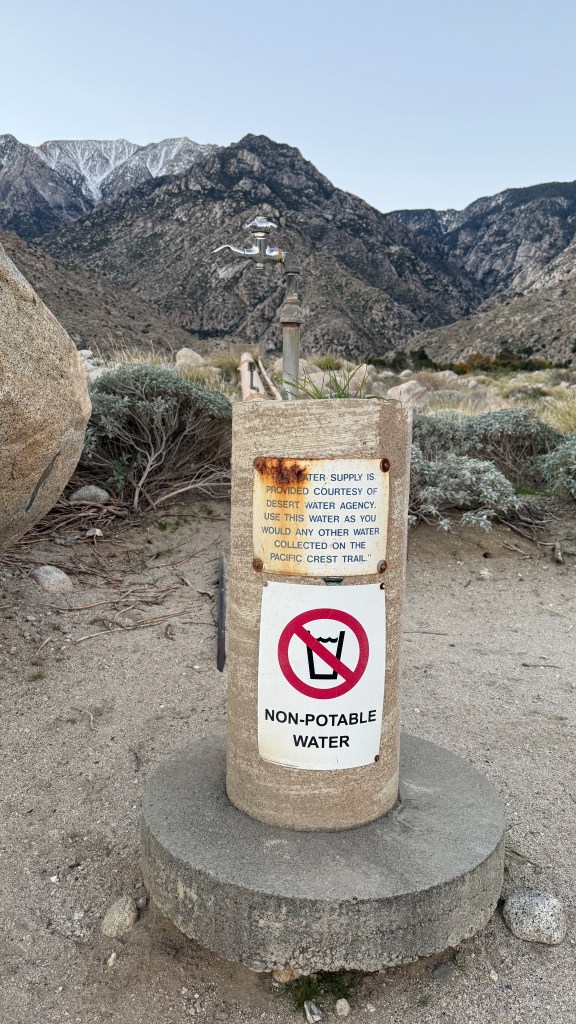 A non-potable water spigot near the Pacific Crest Trail, with mountains in the background and signs warning against drinking the water.