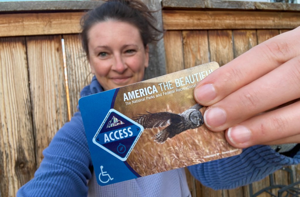 A person holding an 'America the Beautiful' access card featuring an owl, standing in front of a wooden fence.