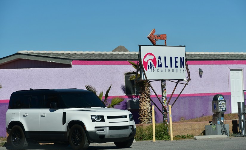 A white SUV parked in front of a colorful purple building with a sign that reads 'ALIEN CATHOUSE', featuring an arrow pointing in a specific direction.