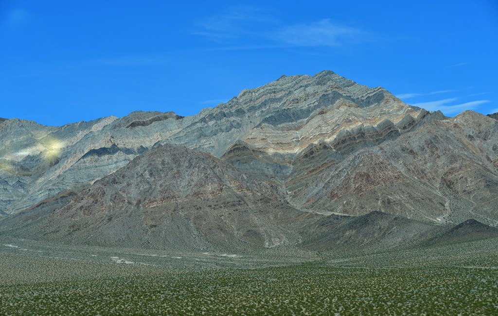 A panoramic view of rugged mountains with layered rock formations against a clear blue sky.