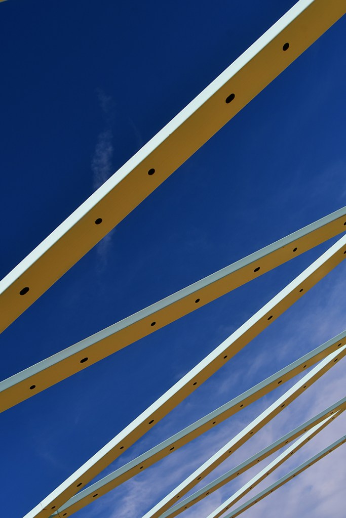 Abstract view of yellow beams against a bright blue sky with a few clouds.