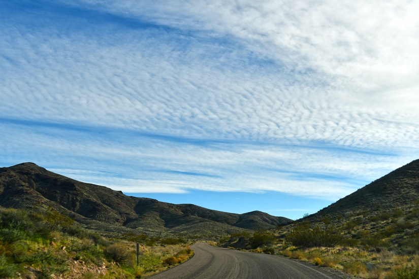 A winding road through a mountainous landscape with blue skies and textured clouds.