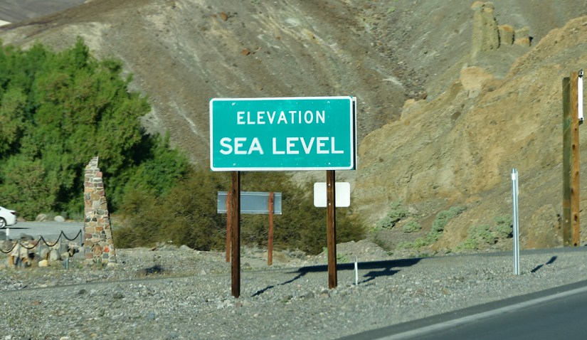 Road sign indicating elevation at sea level with surrounding rocky terrain.