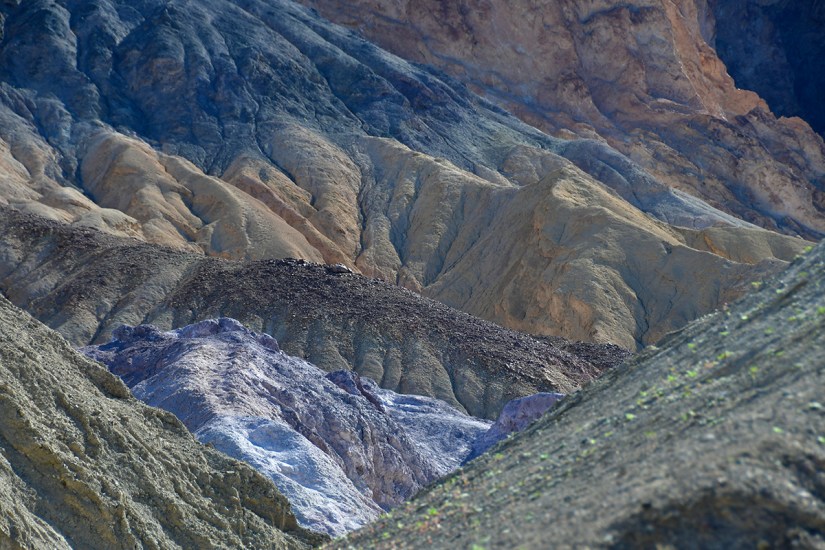 A landscape of colorful, rugged mountains showcasing varied geological formations and textures in shades of brown, blue, and gold.