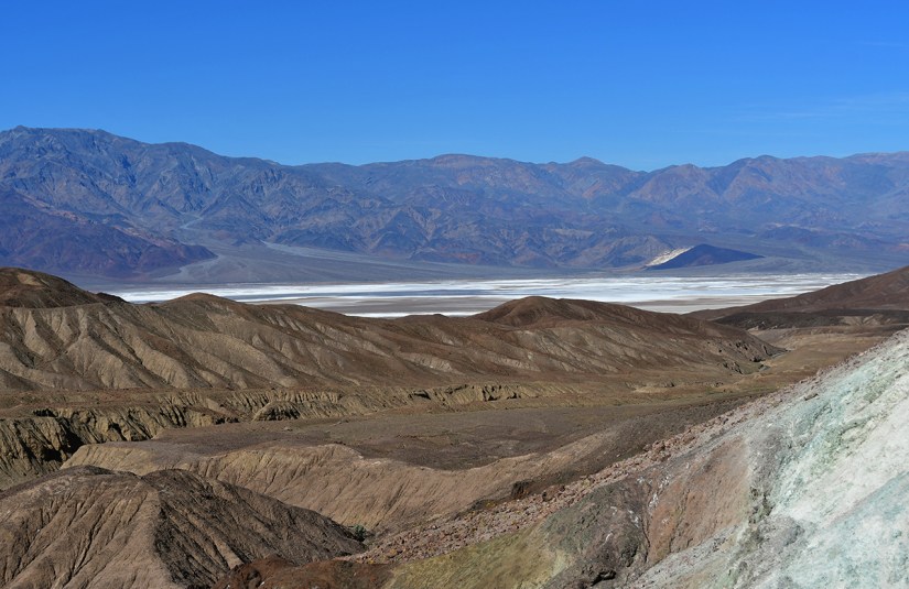 Panoramic view of arid mountains with a salt flat in the distance under a clear blue sky.