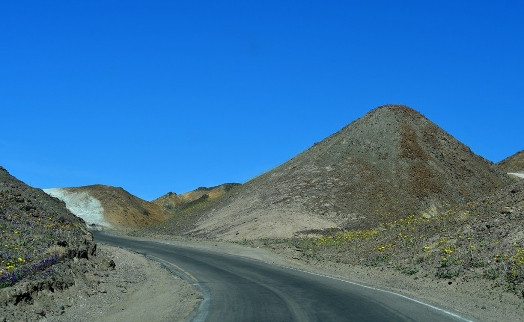 A winding road through a desert landscape with colorful hills under a bright blue sky.