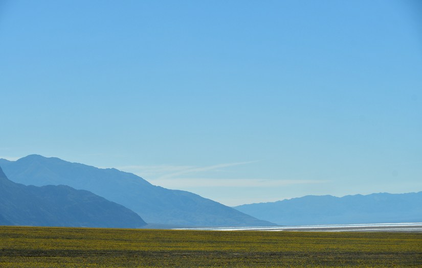 A panoramic view of a vast desert landscape with distant mountains under a clear blue sky.