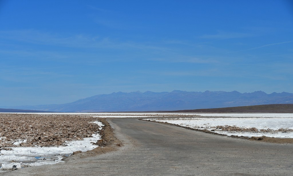 A winding road leading through a salt flat landscape with mountains in the background under a clear blue sky.
