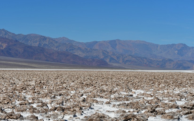 A view of a vast salt flat with rocky formations, set against a backdrop of mountains under a clear blue sky.