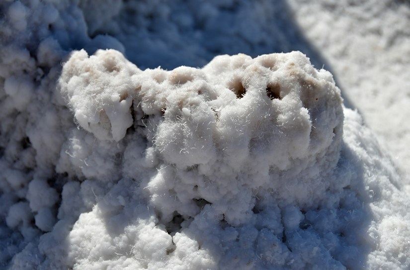 Close-up of a textured, white mineral formation resembling salt crystals, with a rough and fluffy appearance.