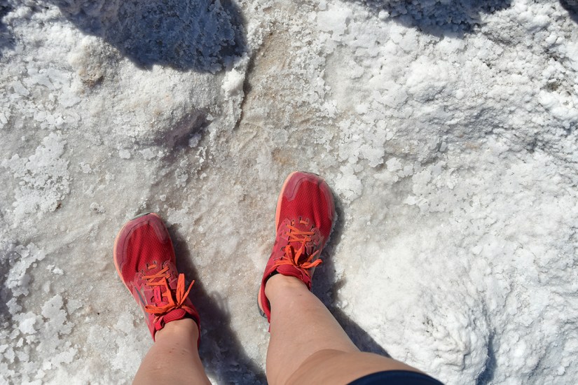 Feet wearing bright red athletic shoes standing on a white, salt-covered surface.