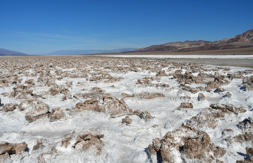 A vast salt flat with rocky formations, set against a clear blue sky and distant mountains.