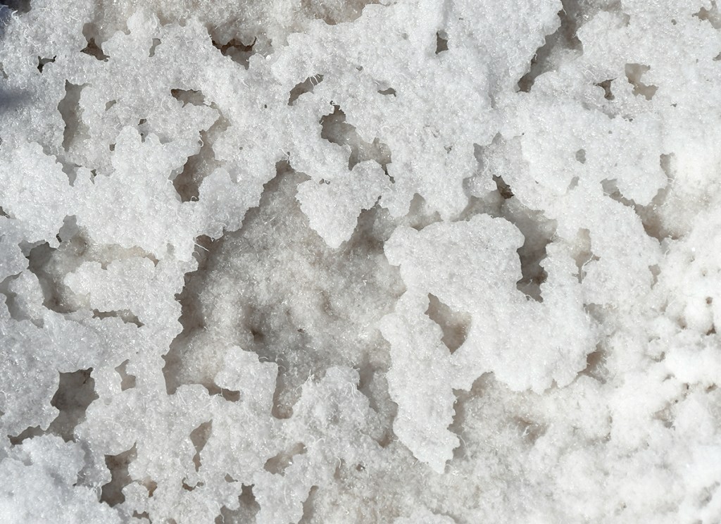Close-up view of textured white snow with uneven shapes and patterns.