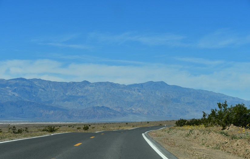 A winding road surrounded by desert landscape and mountains under a clear blue sky.