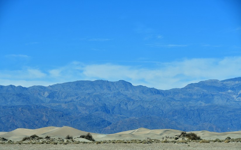 A scenic view of mountains against a clear blue sky, with sandy dunes in the foreground.