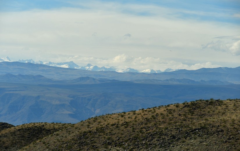 A scenic landscape featuring rolling hills in the foreground and distant snow-capped mountains beneath a cloudy sky.