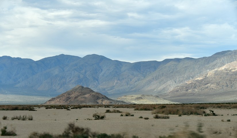 Wide view of a desert landscape featuring mountains in the background and sparse vegetation in the foreground.