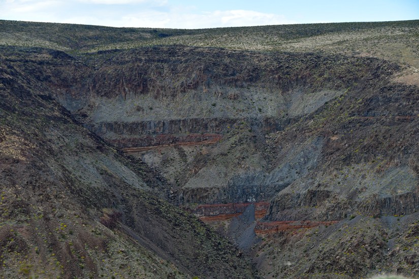 A view of a rugged canyon landscape showcasing layered rock formations and steep slopes, with sparse vegetation on the hillsides.