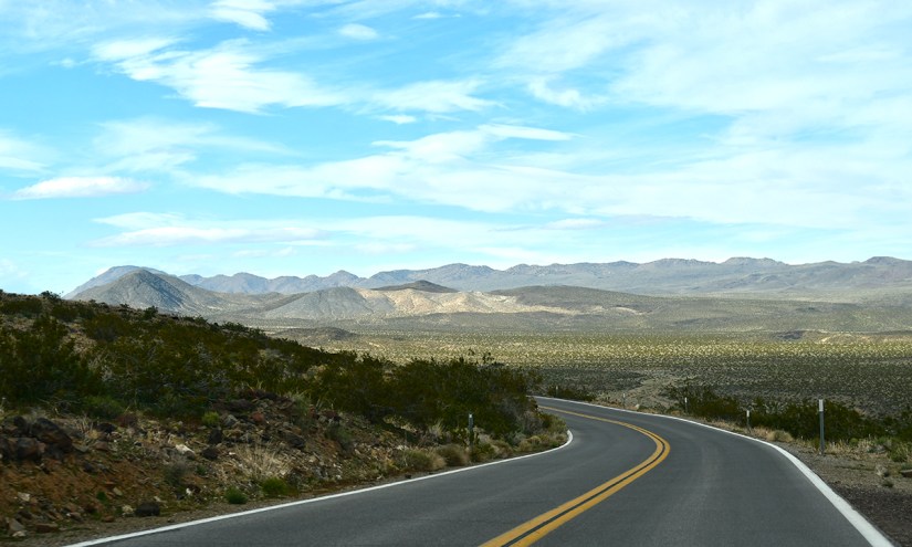 A winding highway through a desert landscape with mountains in the background and a blue sky.
