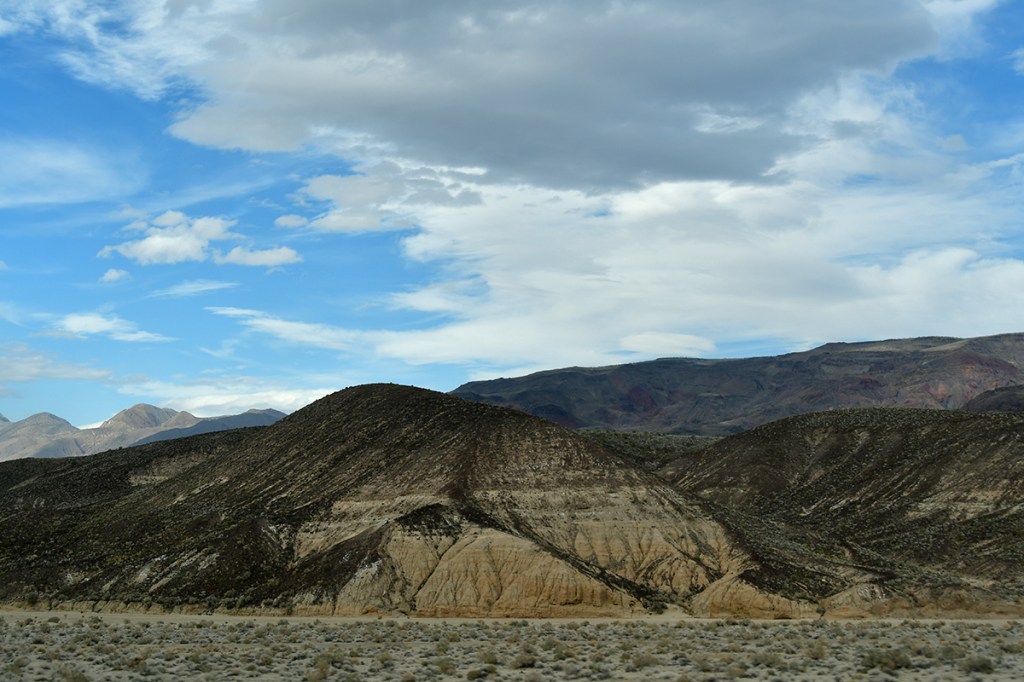 A scenic view of rolling hills and mountains under a partly cloudy sky.