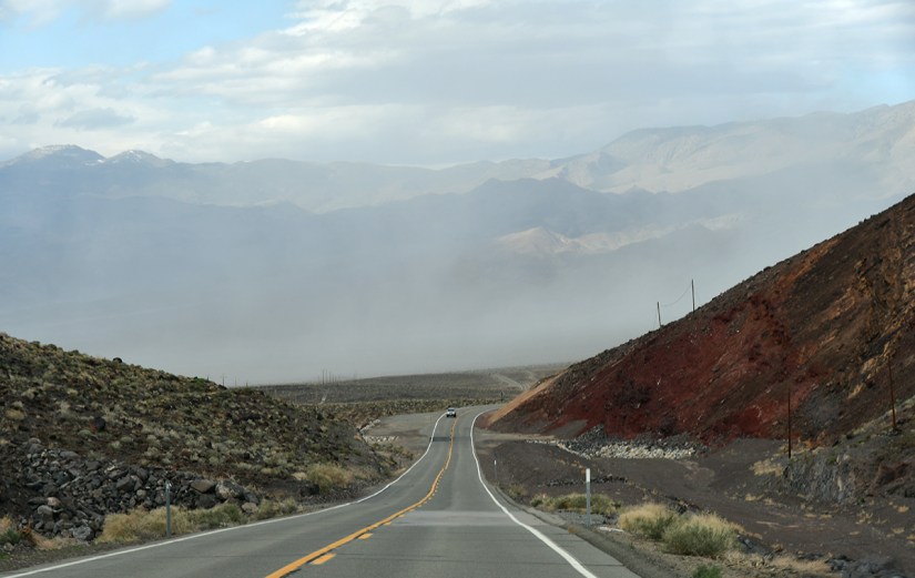 A winding road leads through a mountainous landscape, with mist rising in the background and rocky hills on either side.