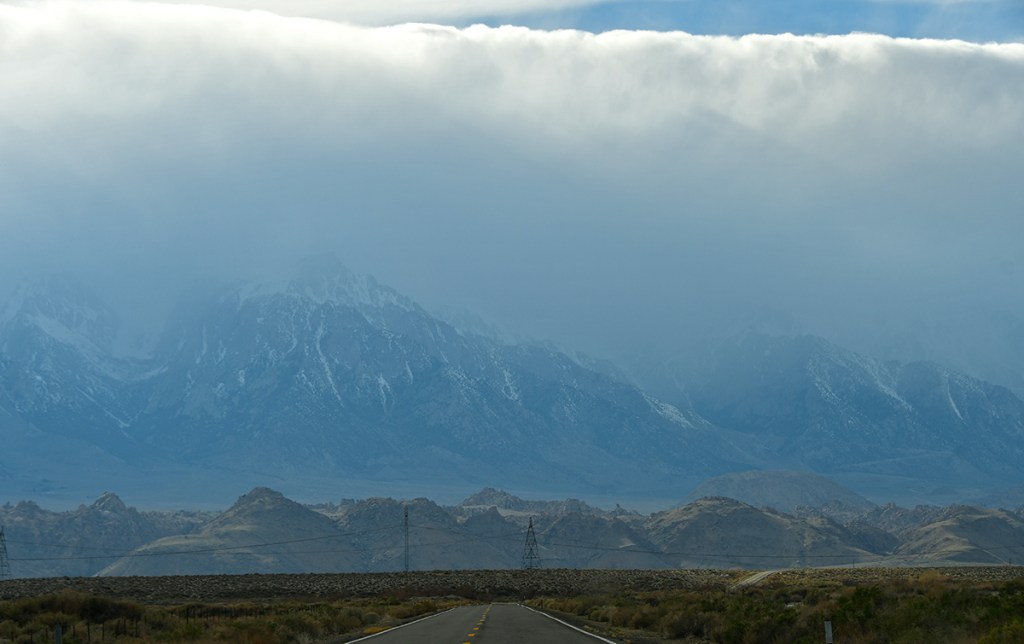 A scenic view of a road leading towards misty mountains partially hidden by clouds, with power lines running alongside.