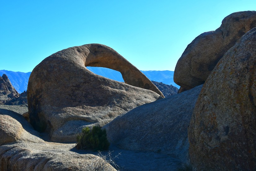 A natural granite rock formation with a distinct arch shape, set against a clear blue sky.