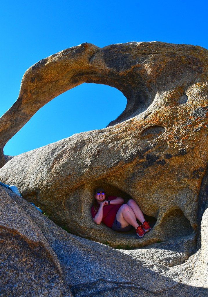 A person sitting inside a natural rock formation with a hole, against a clear blue sky.