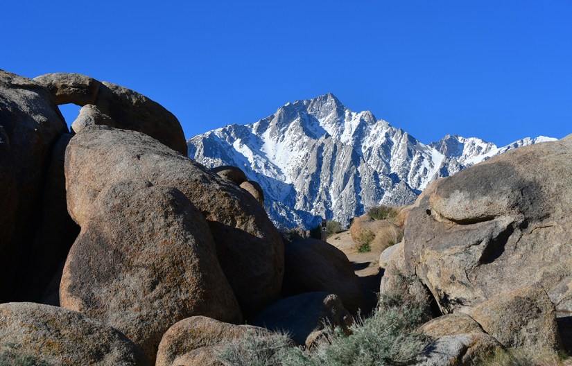 Scenic view of rocky formations with a snowy mountain peak in the background under a clear blue sky.