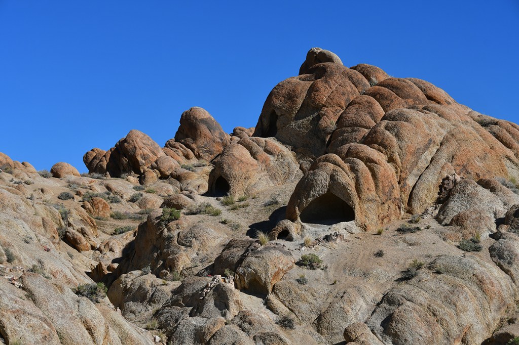 A rugged landscape featuring large, rounded rock formations with a clear blue sky in the background.