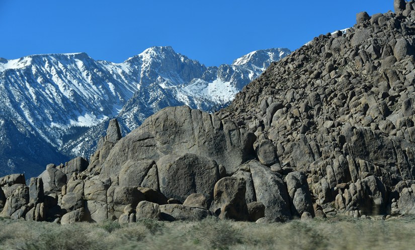 A scenic view featuring rugged boulders in the foreground and snow-capped mountains under a clear blue sky in the background.