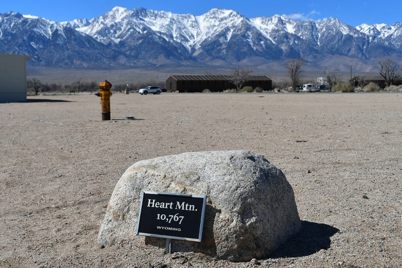 A rock with a sign marking Heart Mountain at 10,767 feet, set against a backdrop of snow-capped mountains in Wyoming.
