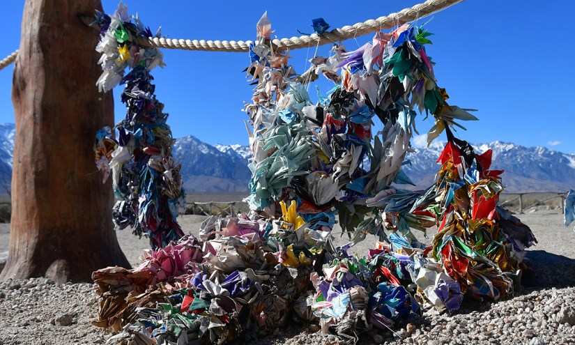 A close-up view of colorful paper cranes hanging from a rope against a backdrop of snow-capped mountains and clear blue sky.