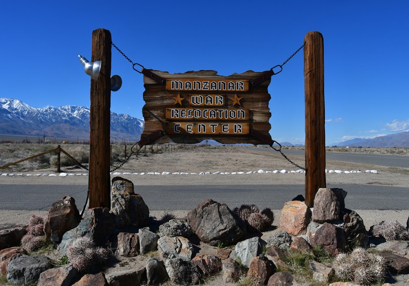 Sign for the Manzanar War Relocation Center with mountains in the background and a clear blue sky.