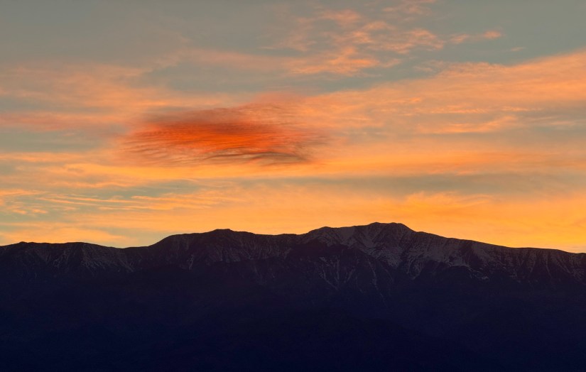 Silhouette of mountains against a colorful sunset sky with orange and pink clouds.