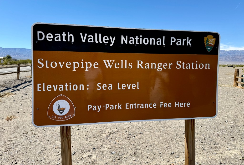 Sign for Stovepipe Wells Ranger Station in Death Valley National Park, indicating elevation at sea level and park entrance fee details.