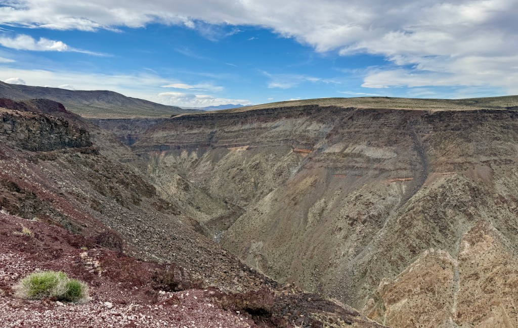A panoramic view of a deep canyon with layered rock formations, contrasting colors, and a clear blue sky.