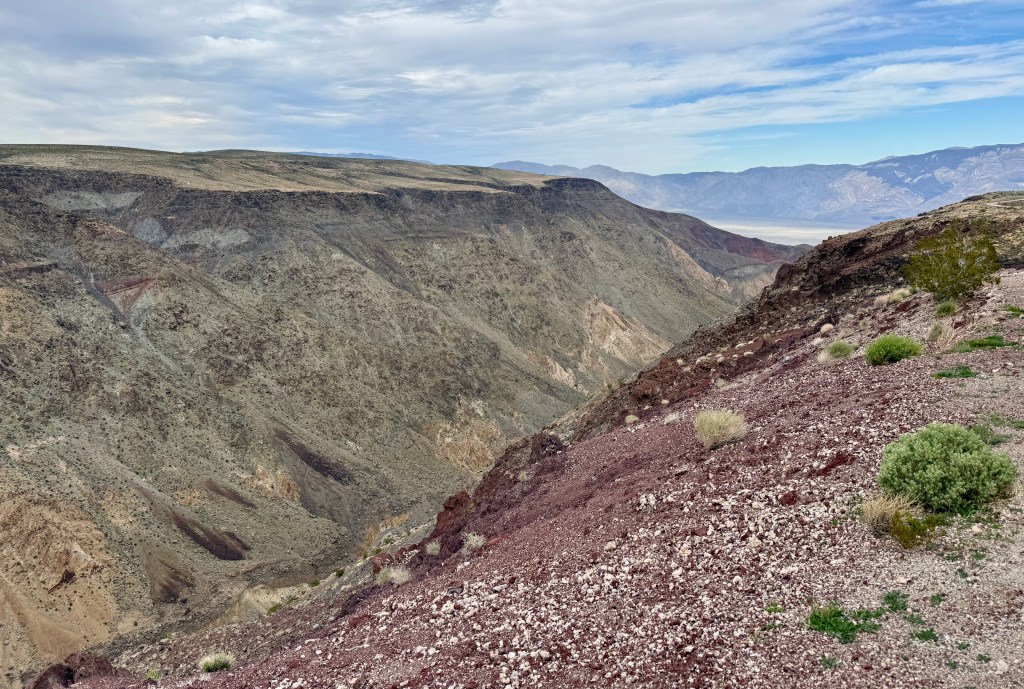 A panoramic view of a rugged canyon landscape featuring varying rock formations and sparse vegetation under a cloudy sky.
