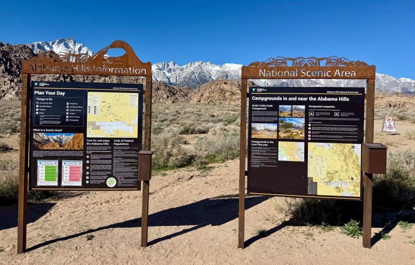 Information signs for Alabama Hills and National Scenic Area against a backdrop of mountains and blue sky.