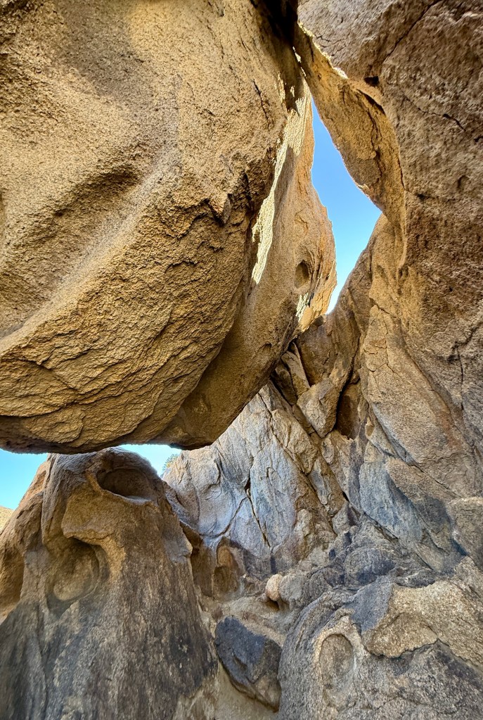 A view of rugged granite rock formations with a narrow opening that reveals a clear blue sky above.