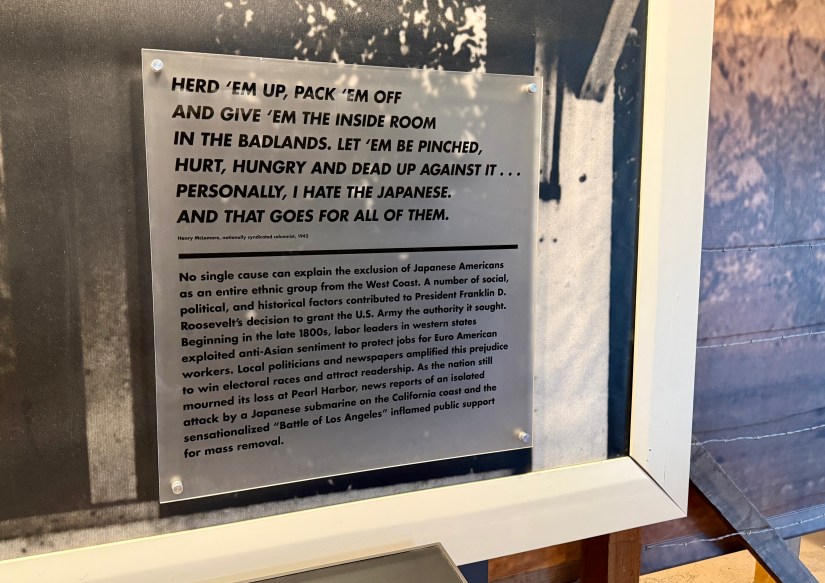 A sign with historical text discussing the exclusion of Japanese Americans during World War II, featuring a quote by Henry McLemore and contextual information on social and political factors behind this action.